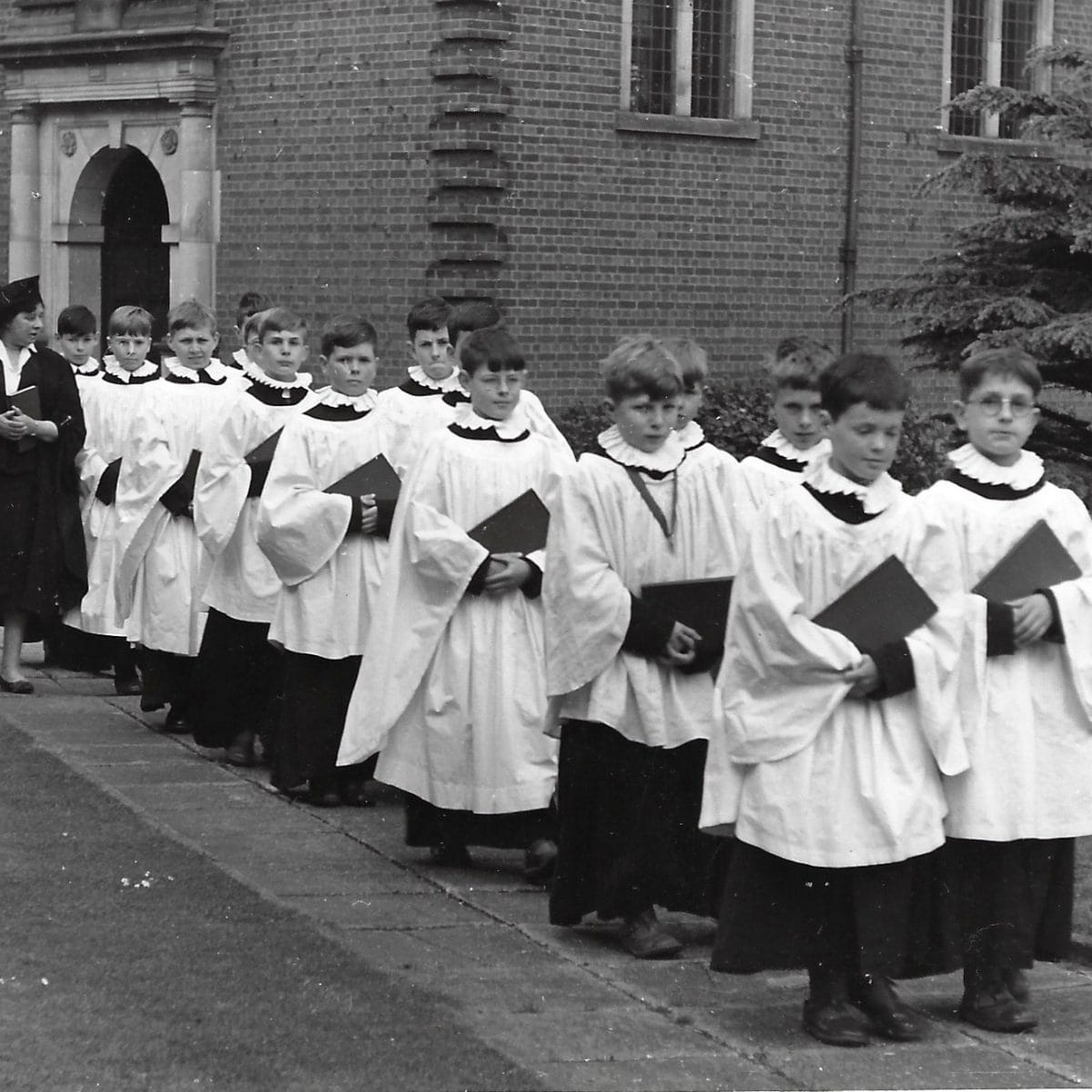 The School Choir dressed in robes walking away from the Chapel in 1959