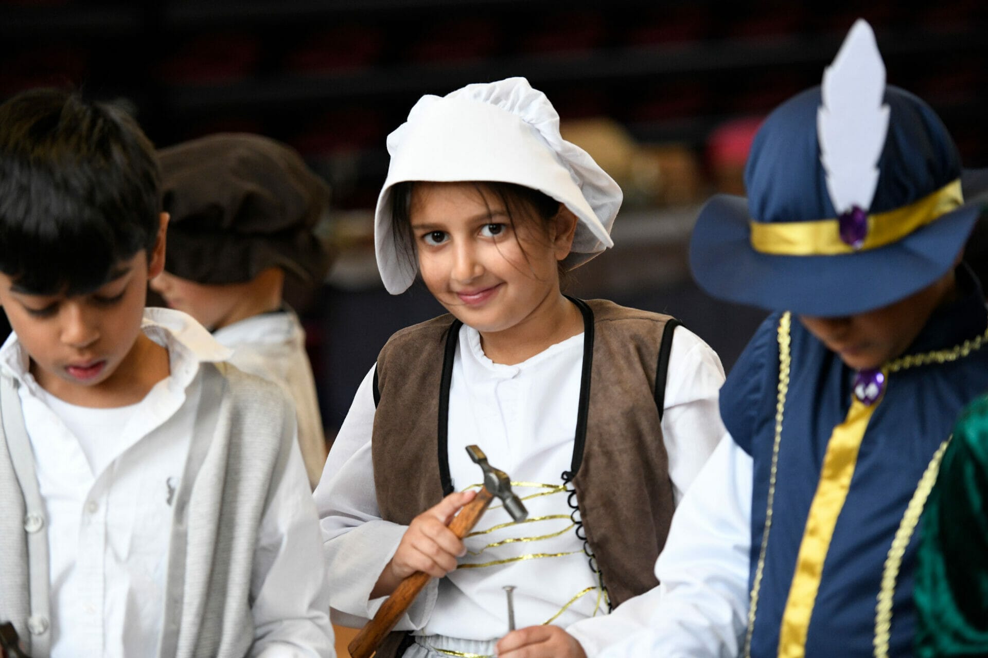 A girl dressed up for Tudor Day uses a hammer and nail in an activity to learn about what tools they used during the Tudor times.