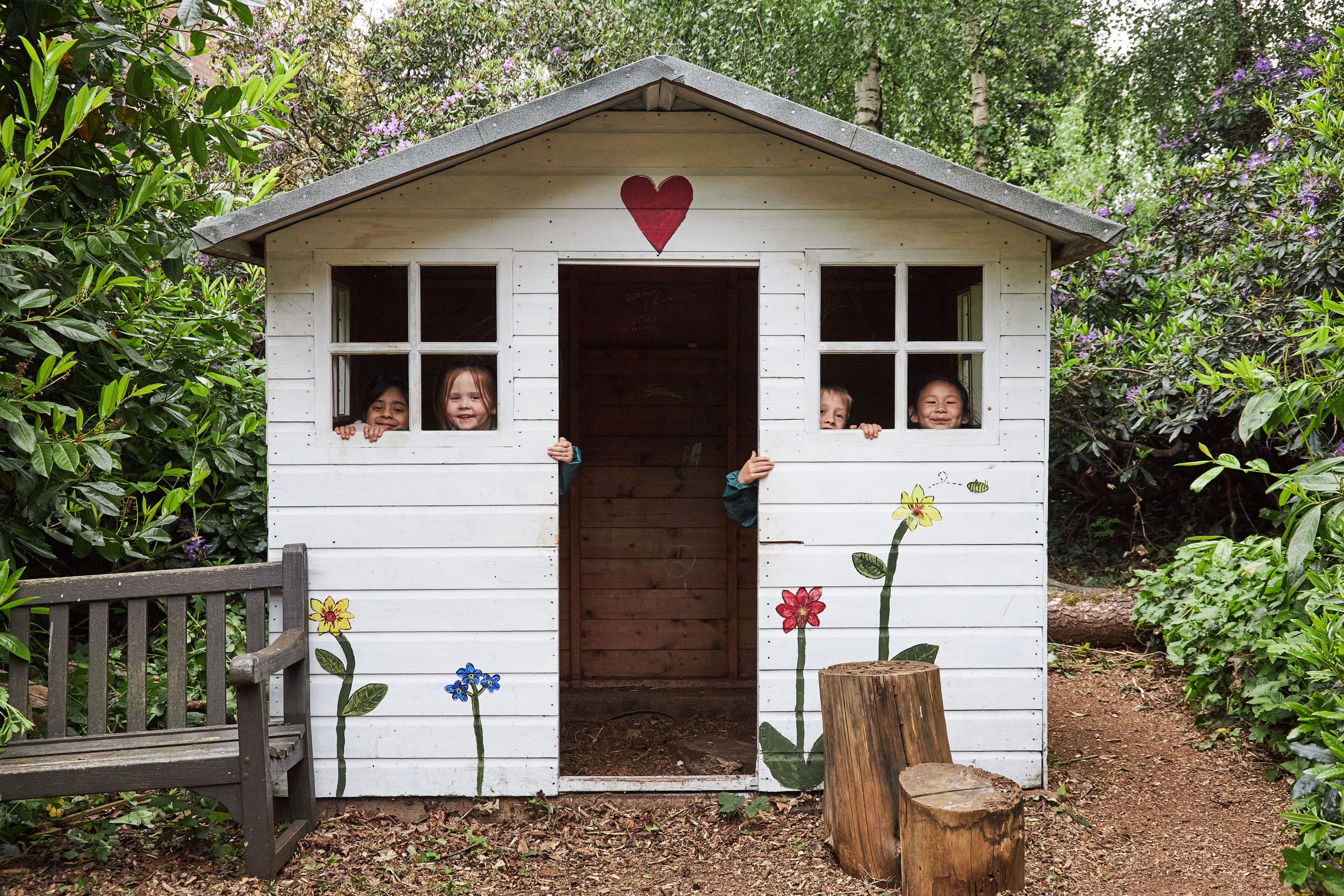 Four children looking through the windows of the forest cottage in Forest School.