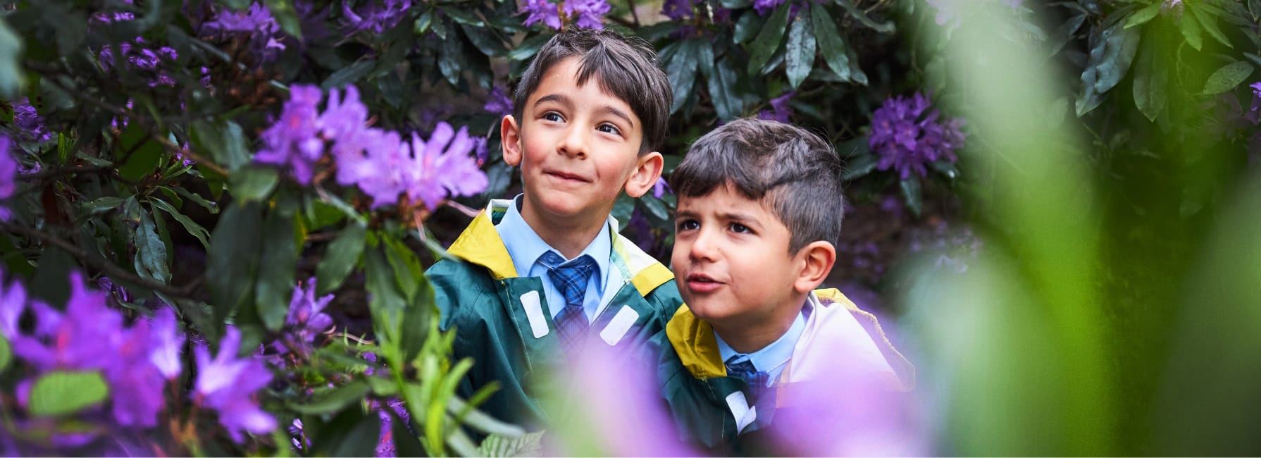 Two Pre-Prep pupils stand amongst flowers during their Forest School class looking curiously.
