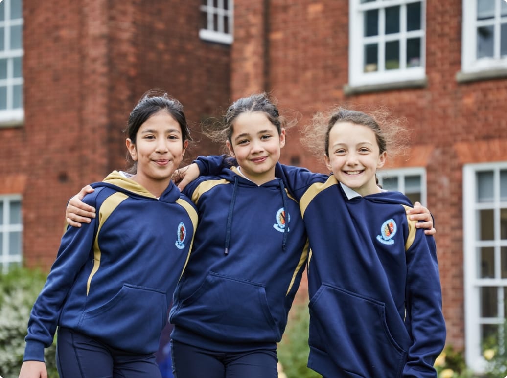 Three girls, dressed in the Blue Coat School PE Kit, stand hugging each other facing the camera