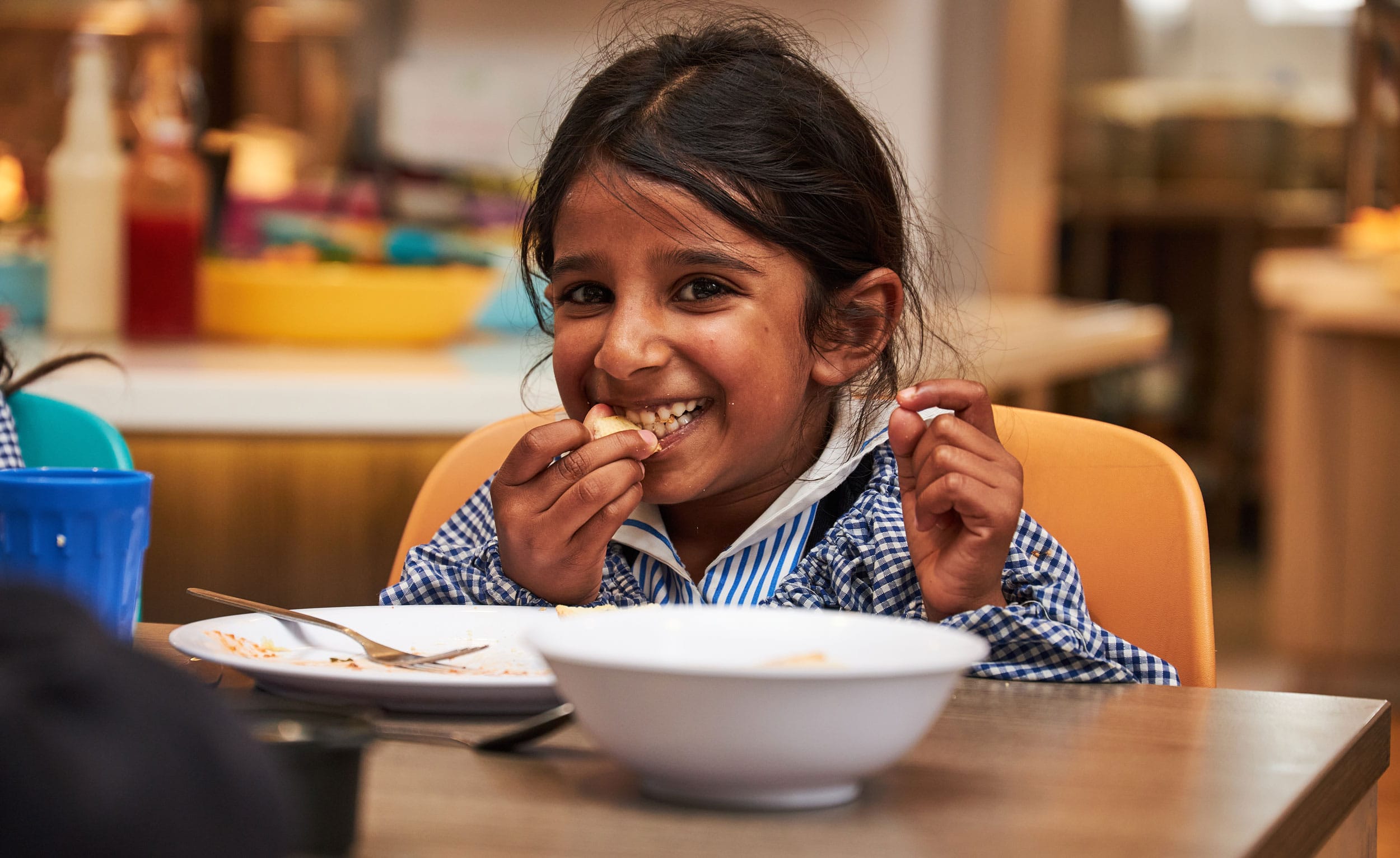 A girl eating from a bowl in The Blue Coat School Dining Hall.
