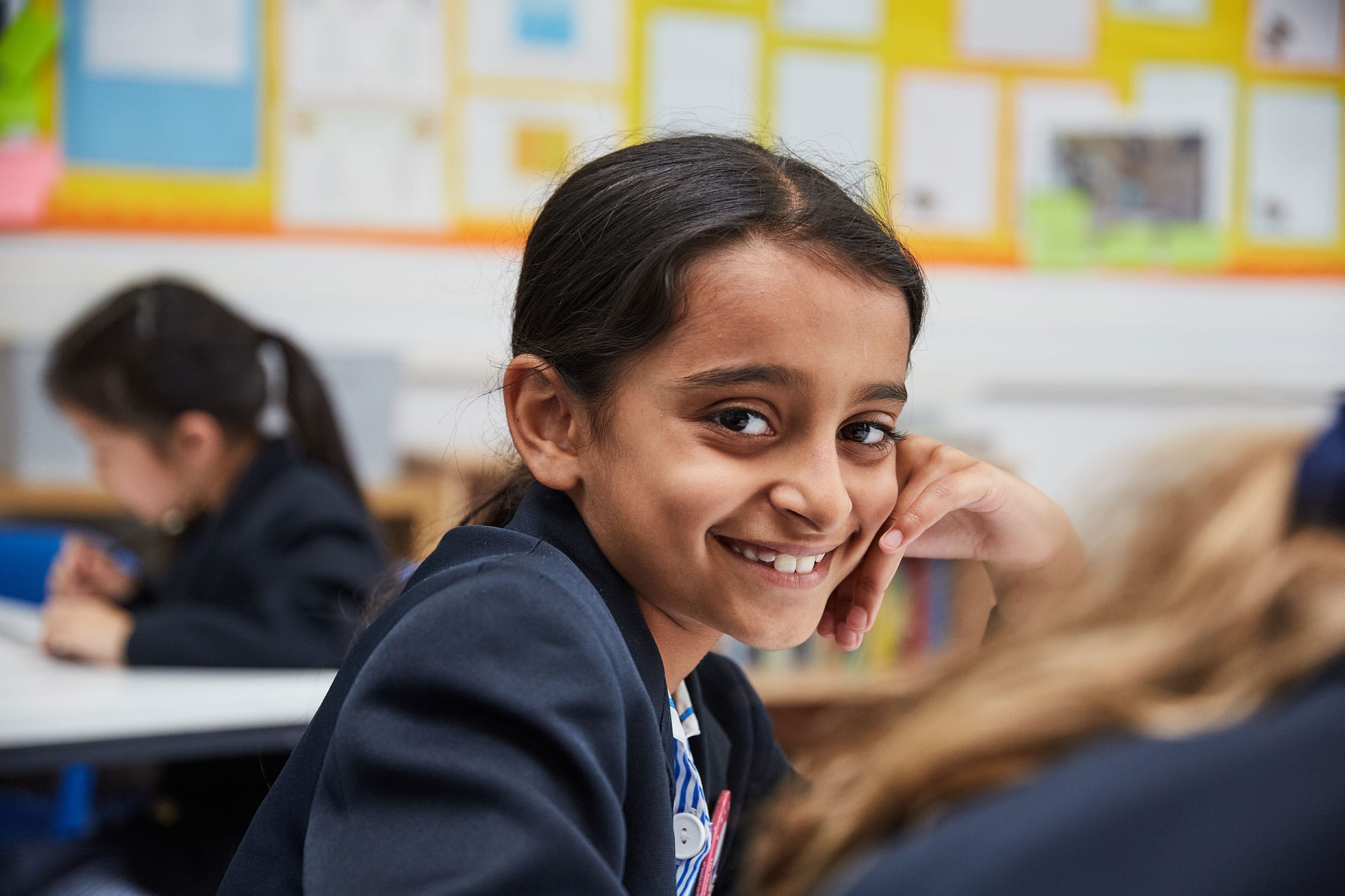 A girl wearing The Blue Coat School uniform sits in an English lesson and smiles at the camera.