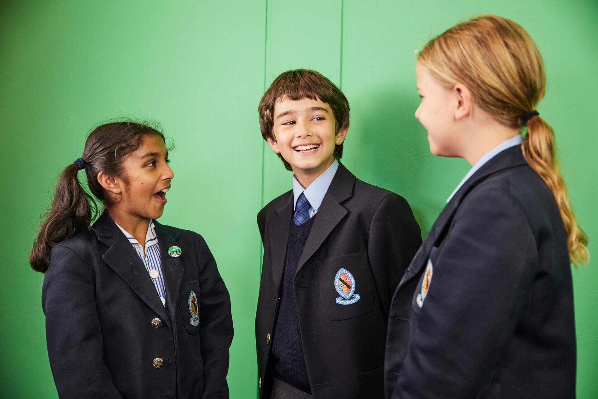 Three pupils in Blue Coat School uniform stand in front of a green screen laughing to one another.