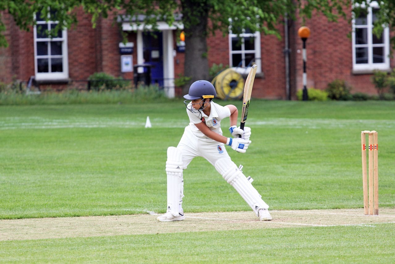 A boy in cricket whites is poised ready to hit the ball in a cricket match.