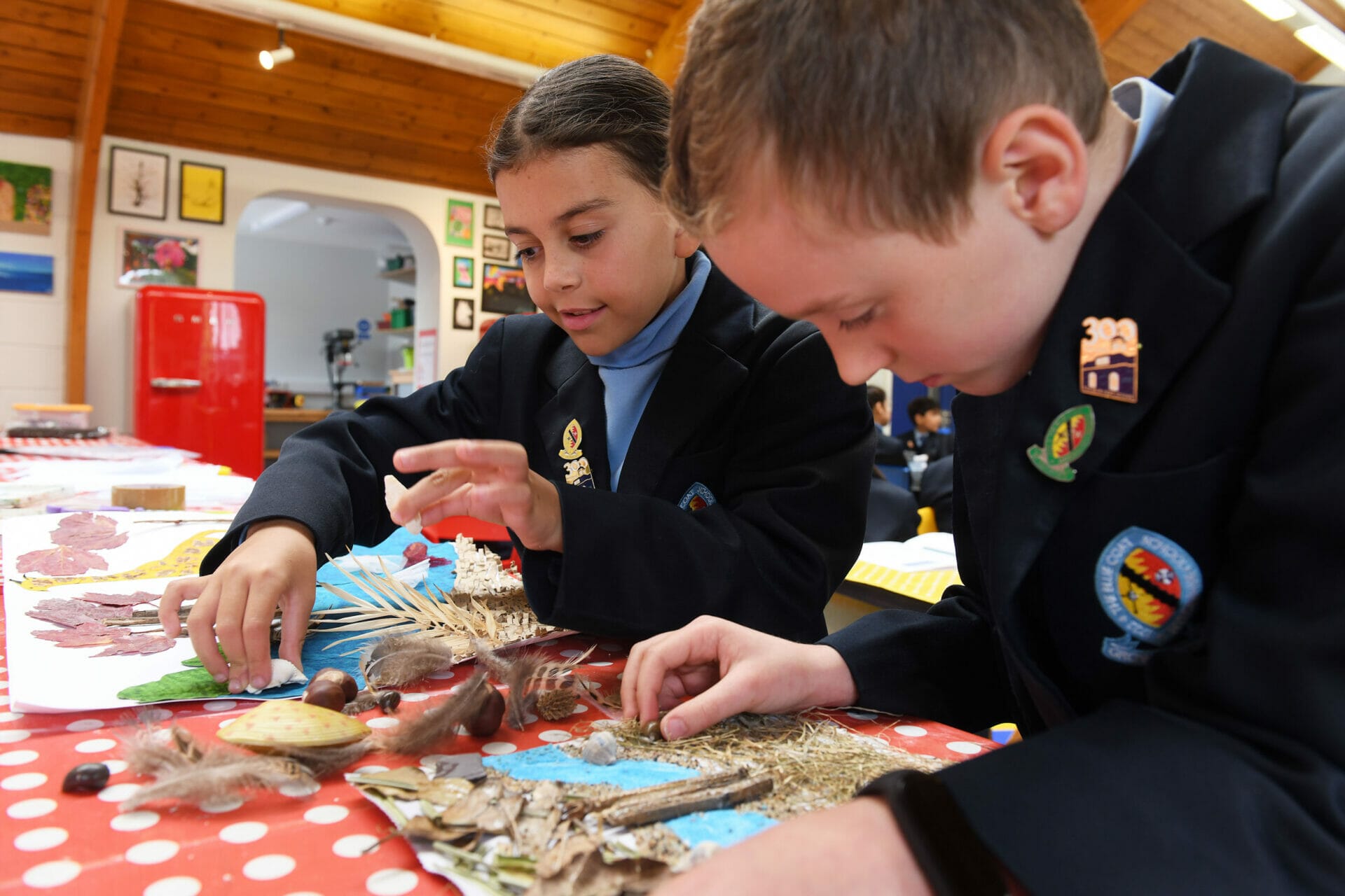 Two pupils stick leaves, conkers and sticks onto a piece of paper to create sustainable artwork.