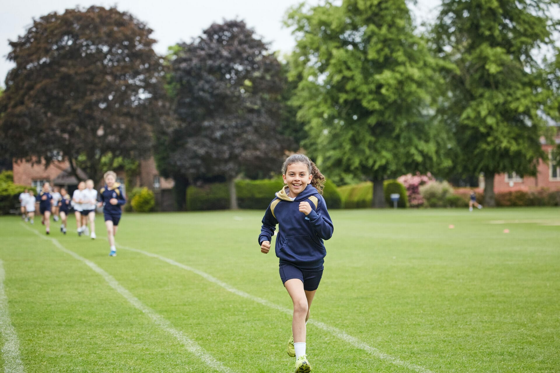 A girl running towards the camera and smiling in a Cross Country lesson.