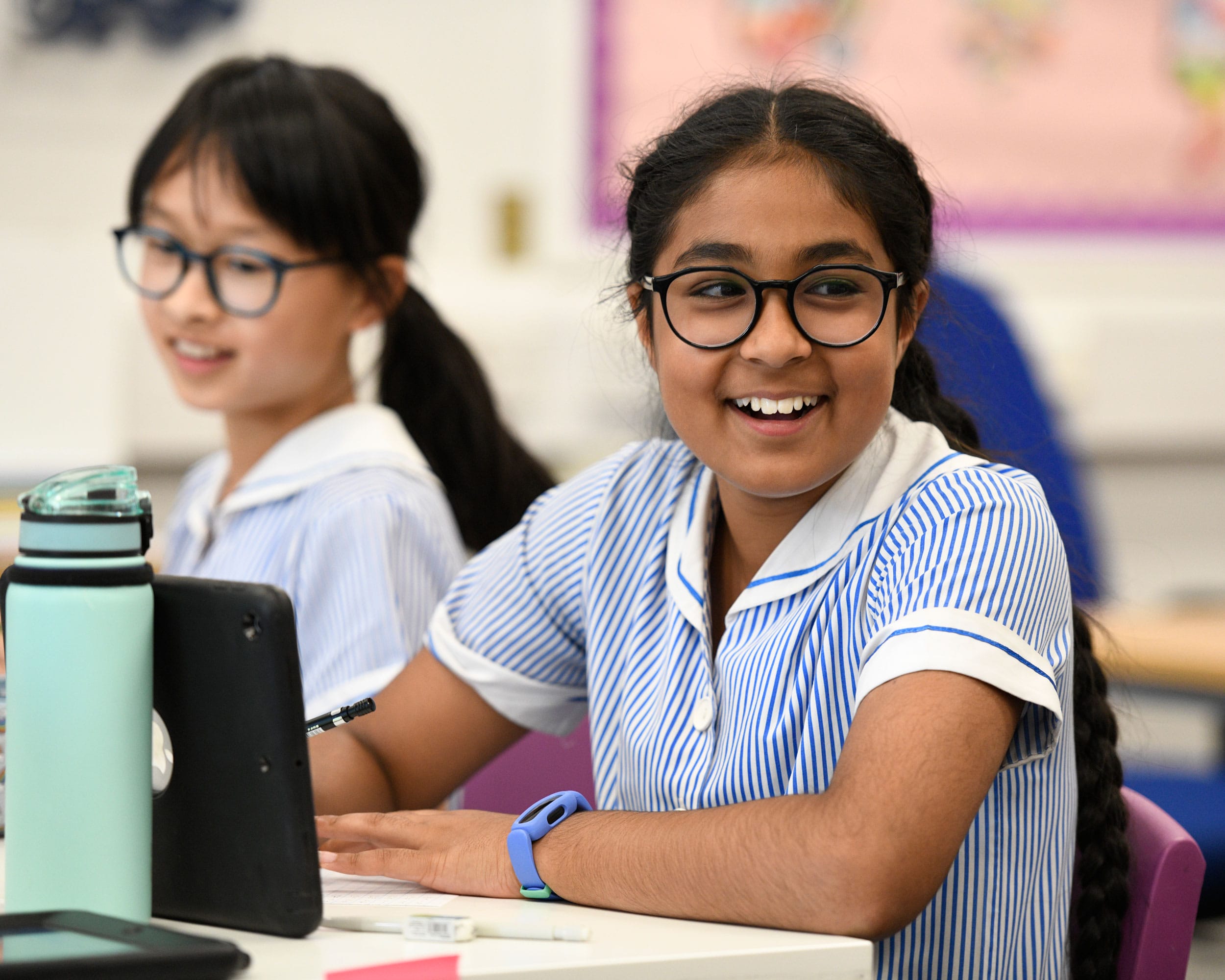 A girl smiles at the camera with an iPad in front of her on the desk.