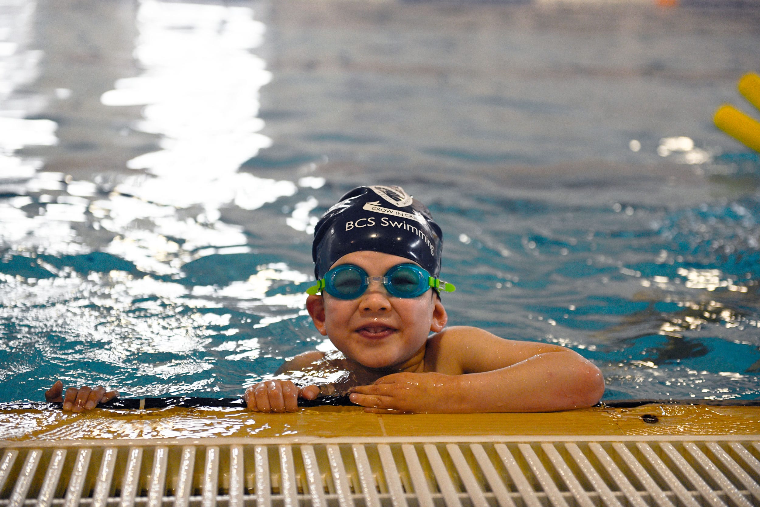 A child rests on the side of the pool at The Blue Coat School and smiles at the camera.