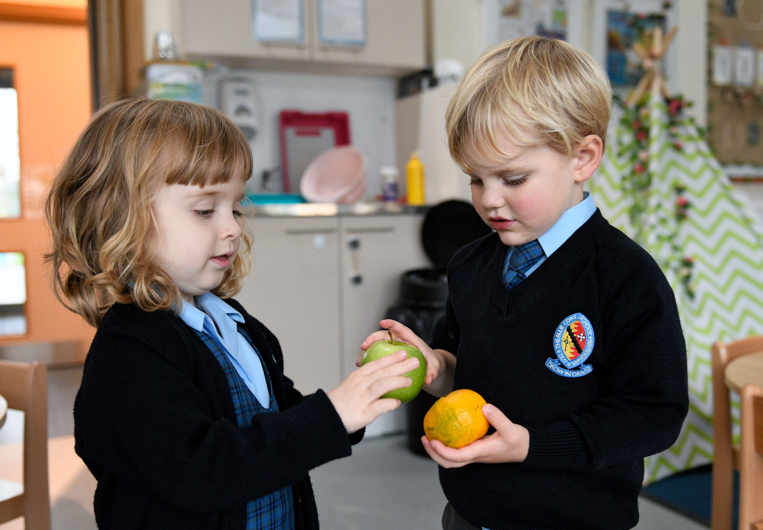 A boy and a girl in Nursery holding an orange and an apple.