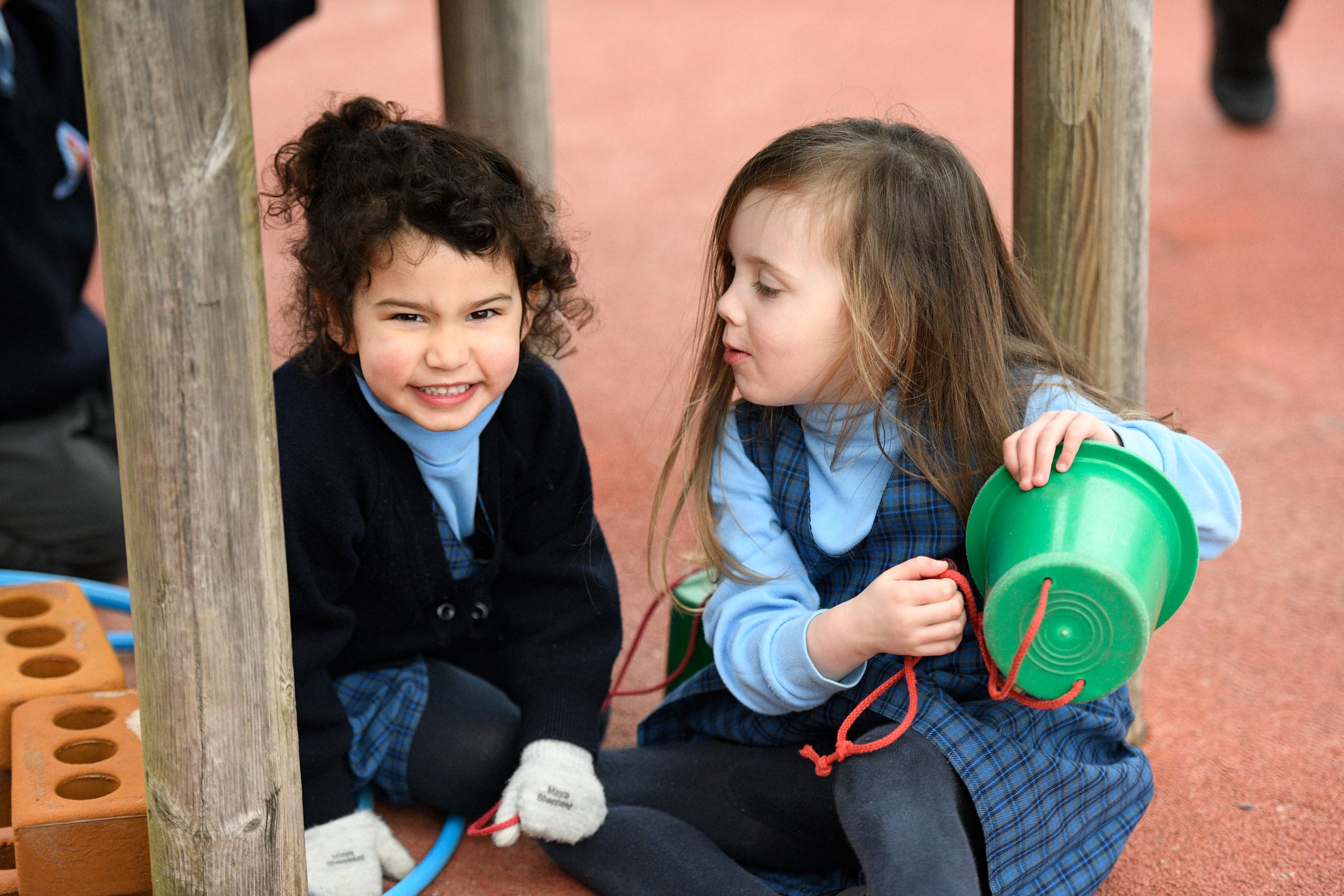 Two Nursery girls playing with a bucket in the playground at The Blue Coat School.