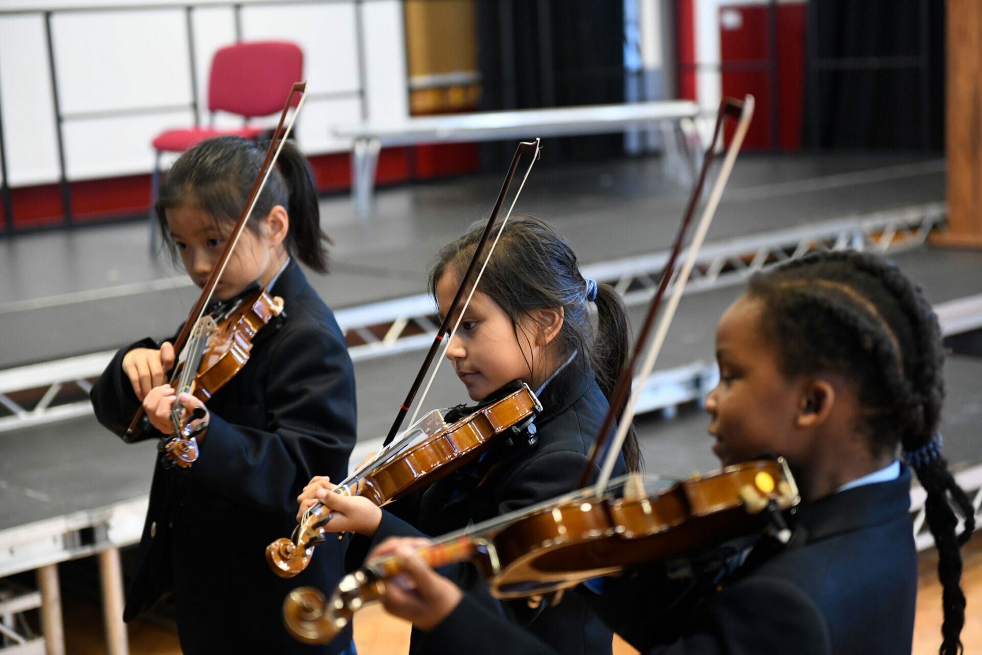 Three girls play violin in the School Hall.