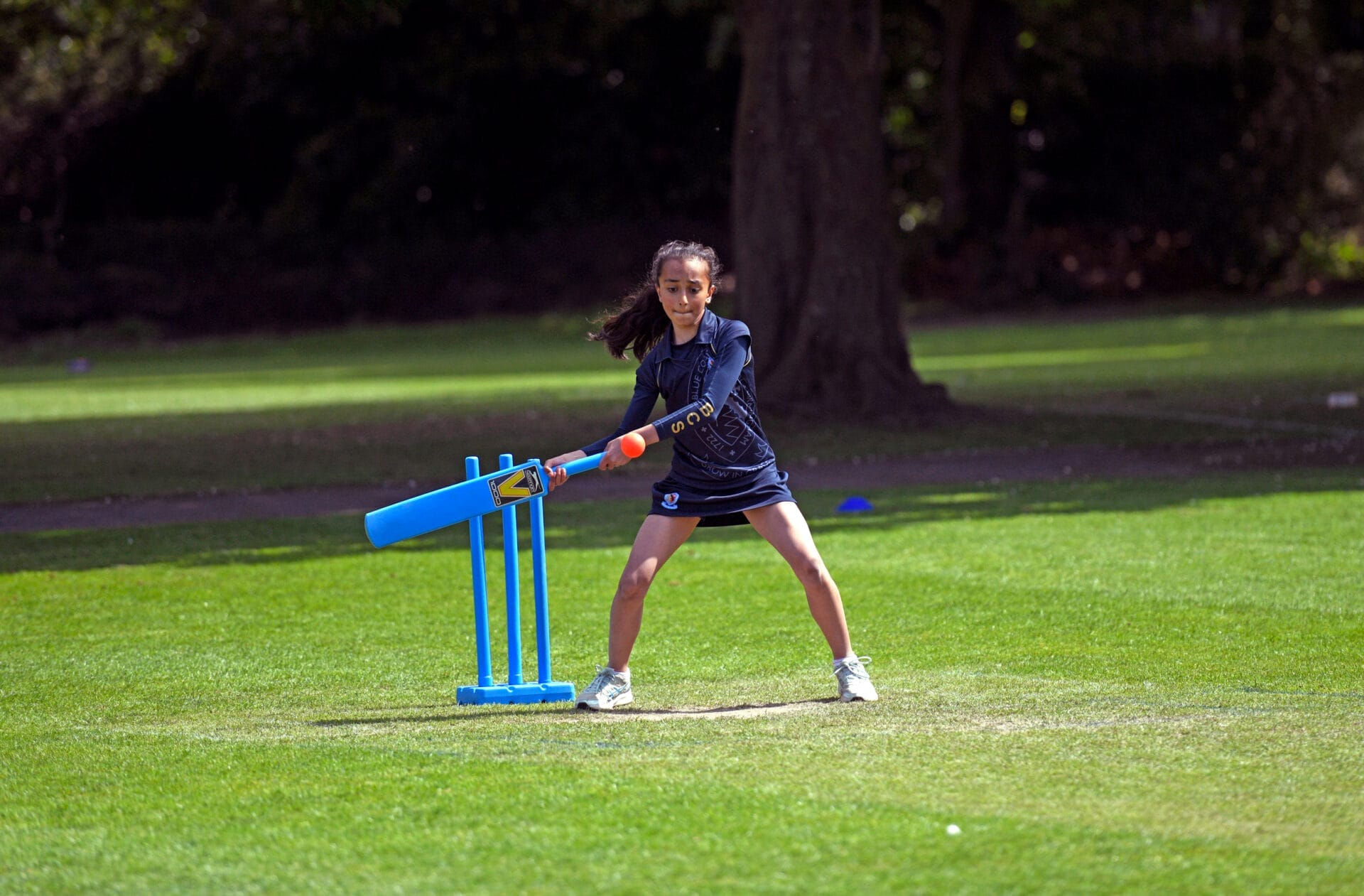 A girl swings to hit the ball in a cricket match.