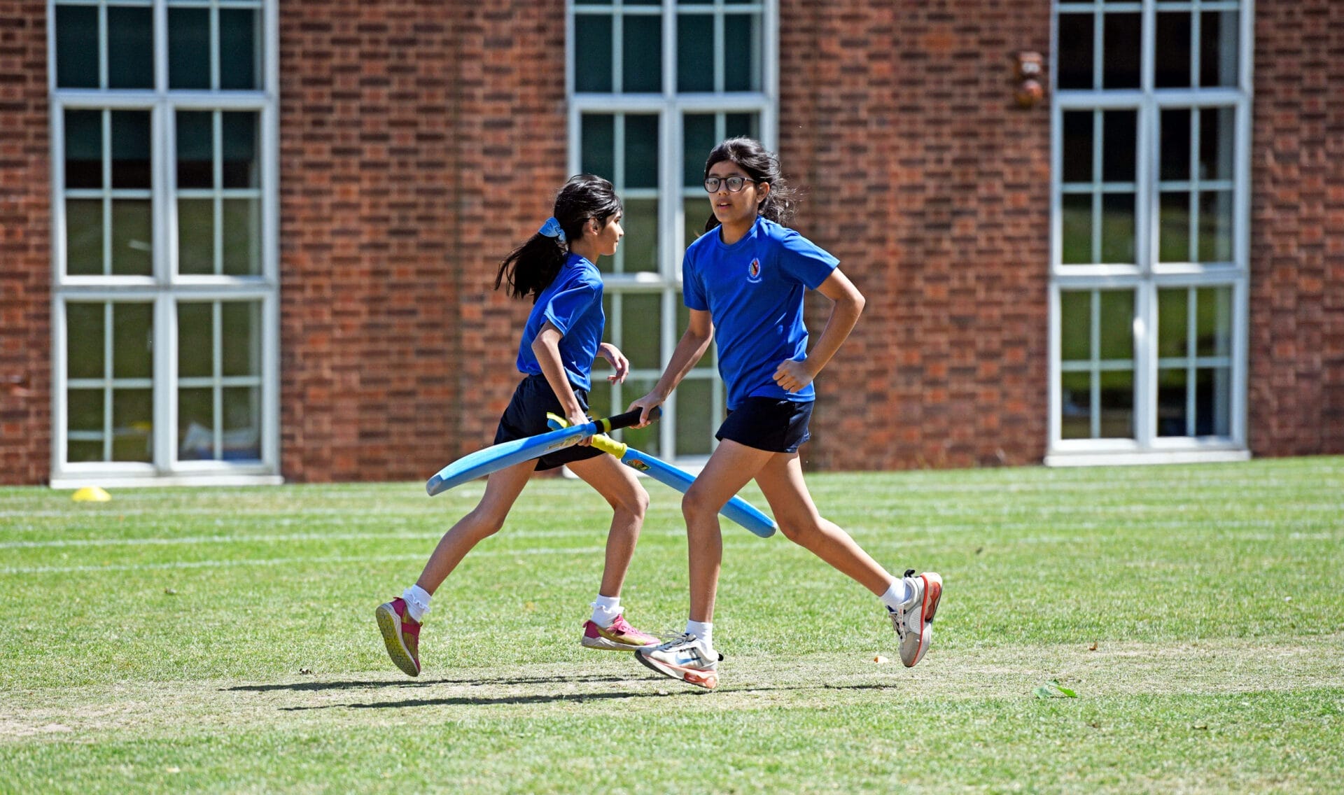 Two girls in blue t-shirts run between the wickets in a House cricket match.