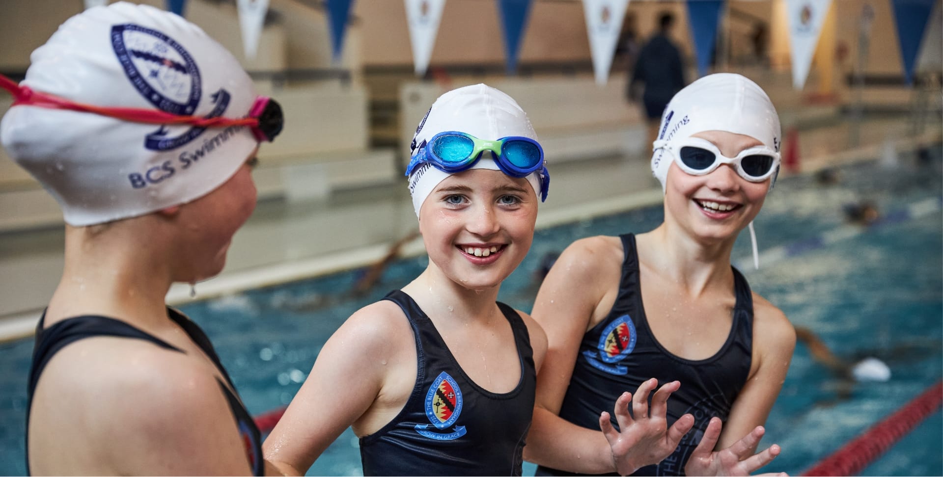 Three girls wearing BCS swimming hats, goggles and swimsuits at the swimming pool at The Blue Coat School.