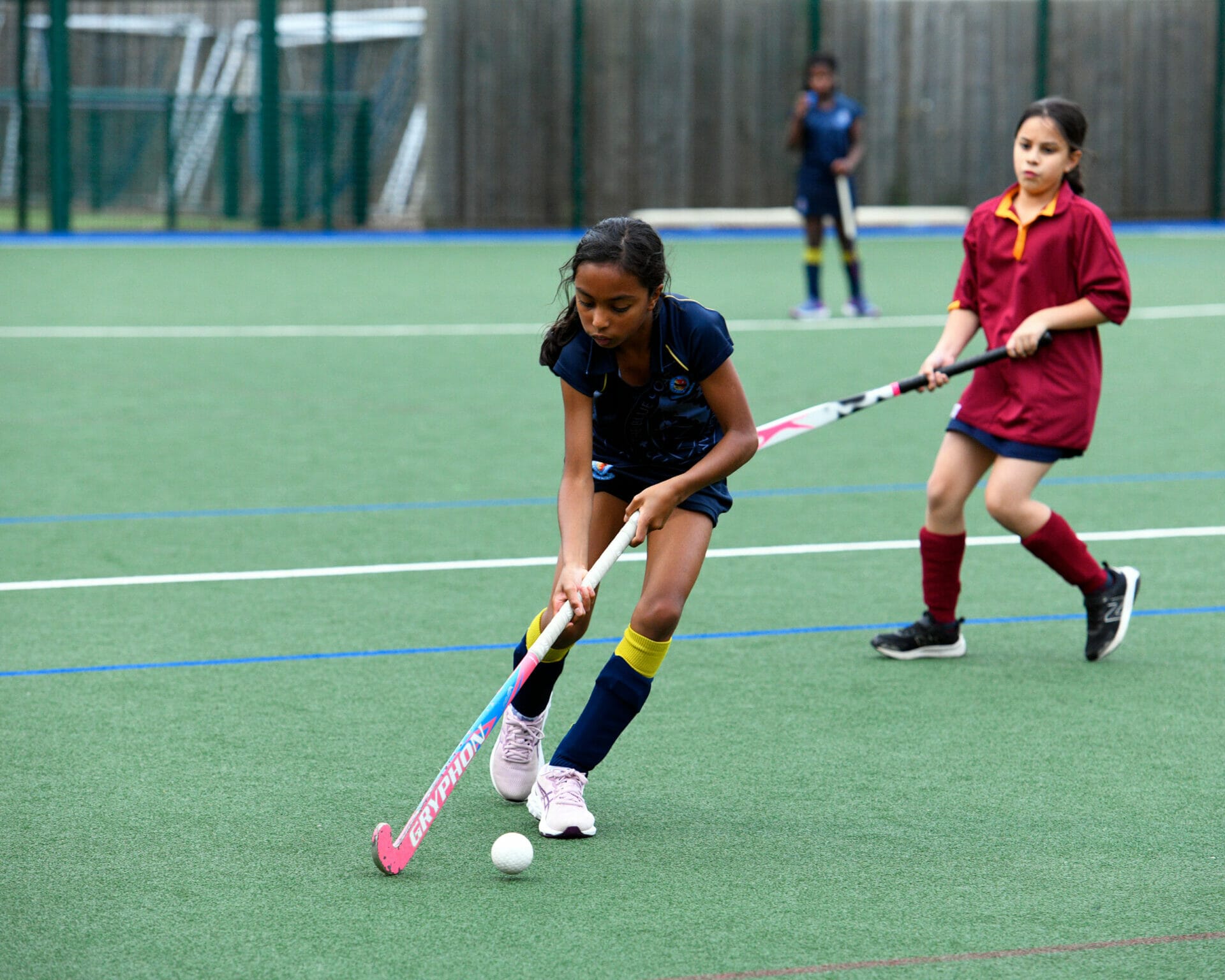 A girl dribbles the ball whilst playing hockey.