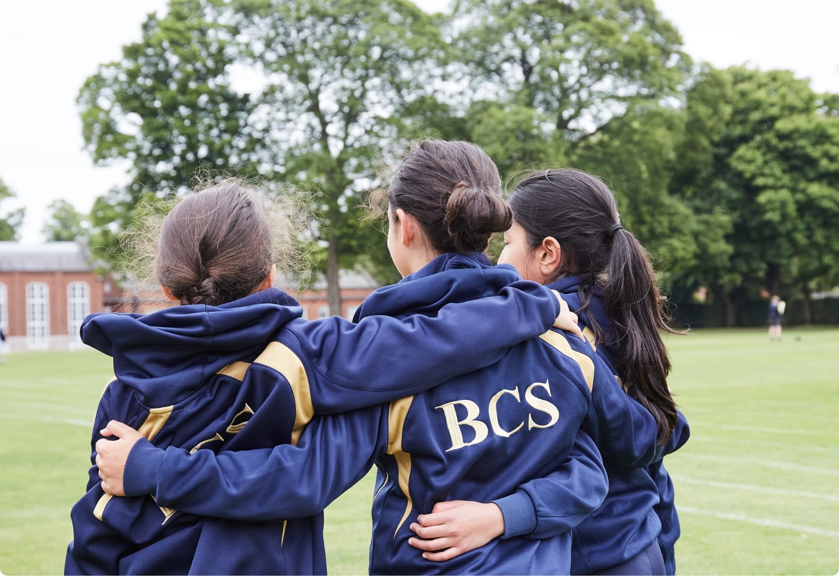 Three girls walking away from the camera with their arms around each other.