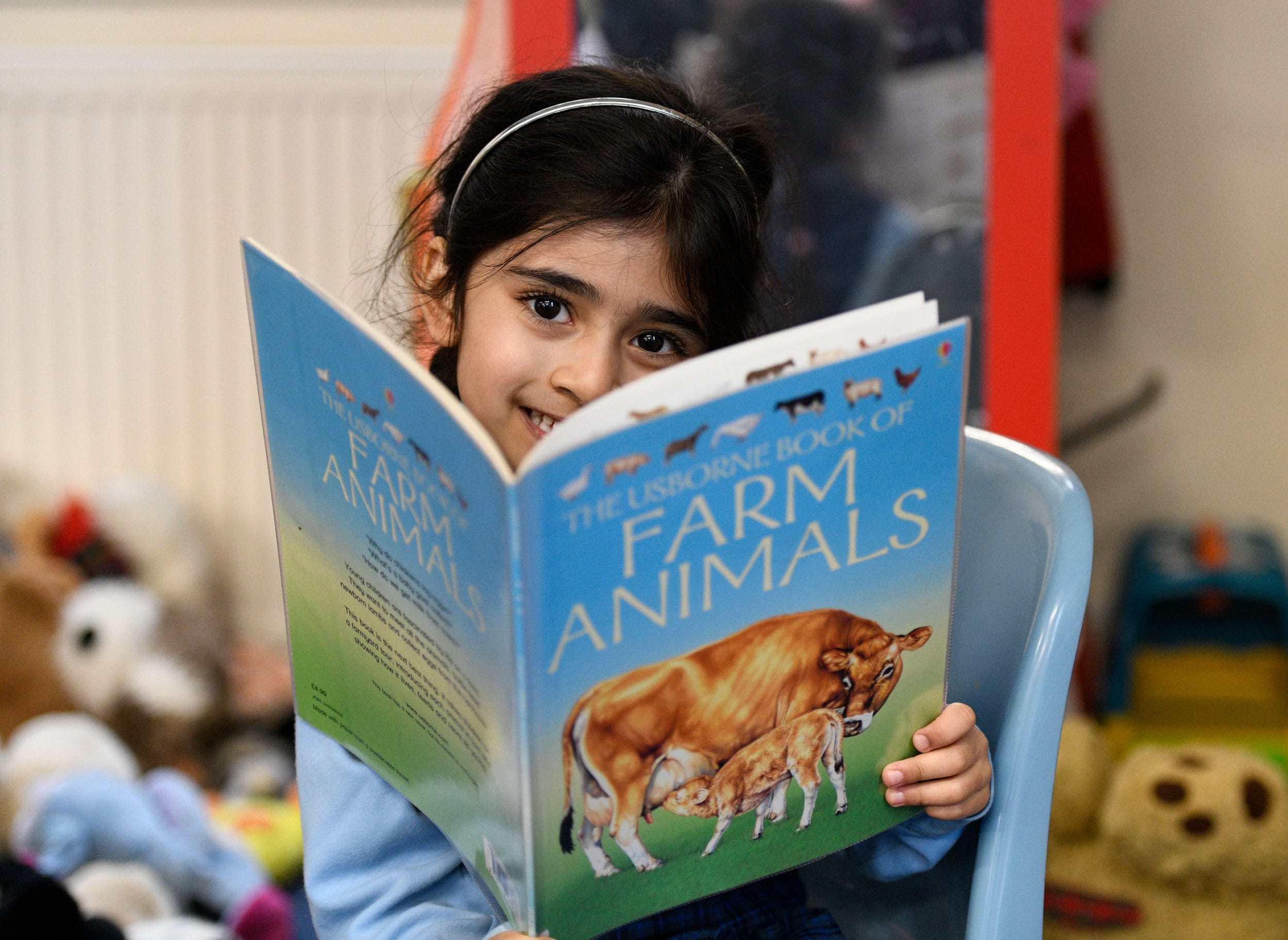 A child looking up above a book about farm animals.