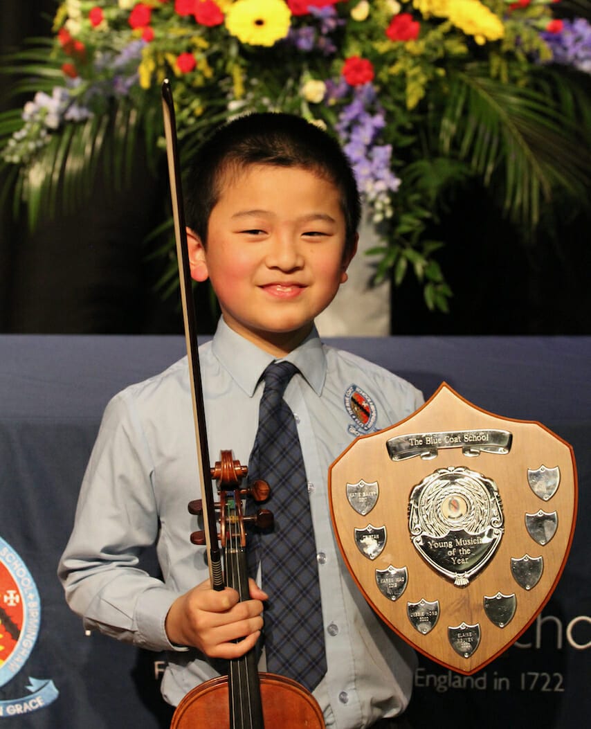A boy holds a violin and the trophy for Young Musician of the Year.